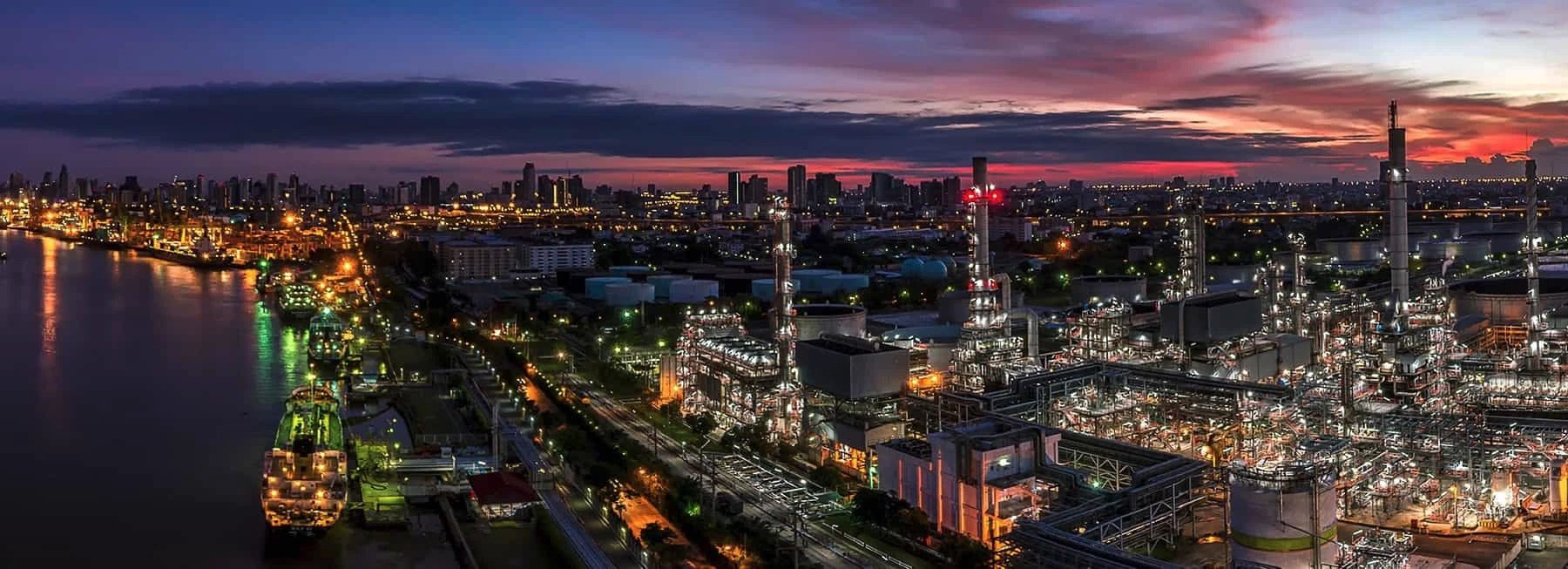 An oil refinery at dusk with a city in the background.