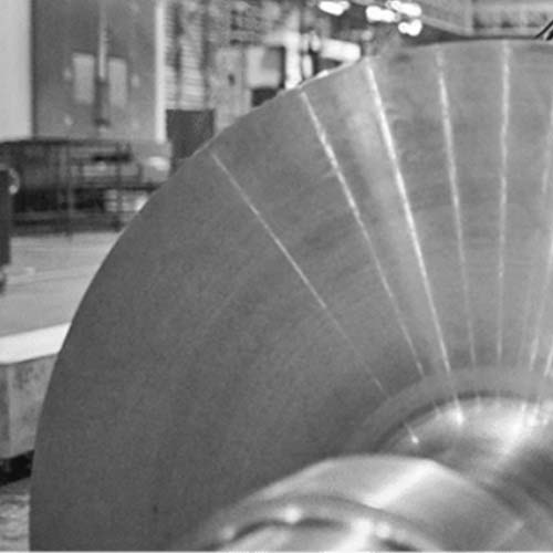 A black and white photo of a metal wheel in a factory.