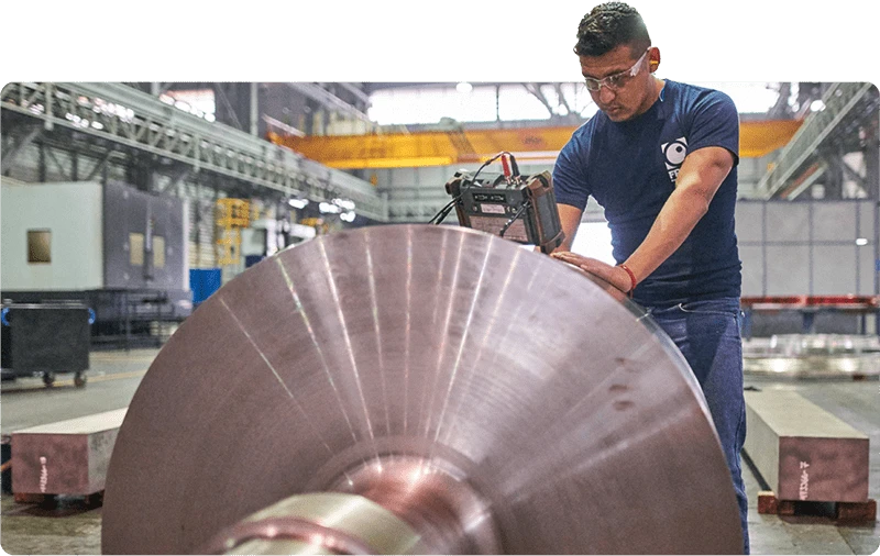 A man working on a large metal roll in a factory.