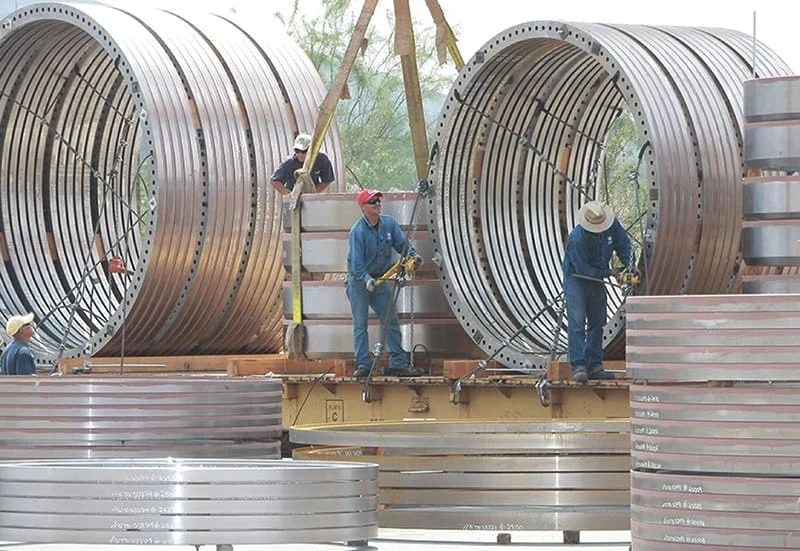 A group of workers are working on a large steel pipe.