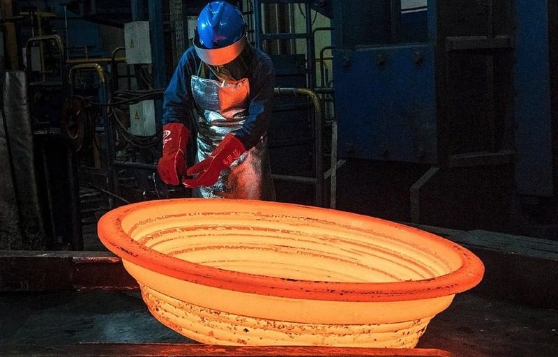 A worker is pouring molten metal into a large bowl.