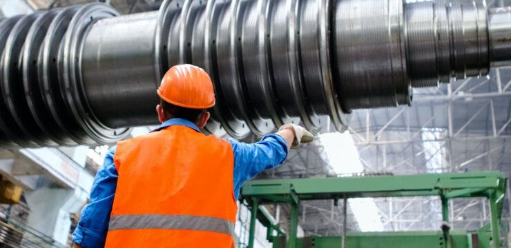 A man in an orange vest is working on a large metal cylinder.