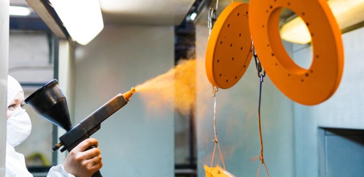 A worker spraying orange paint on a machine.