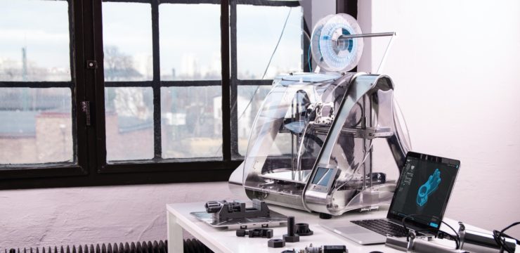 A 3d printer sits on a desk next to a laptop.