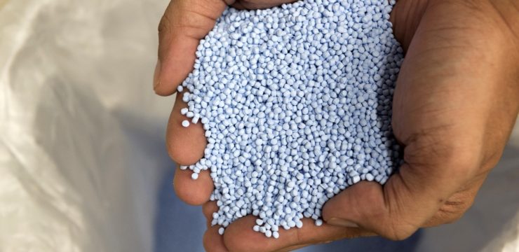 A person is holding a bag of blue granules.