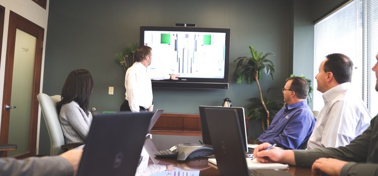 A group of people in a conference room looking at a tv.