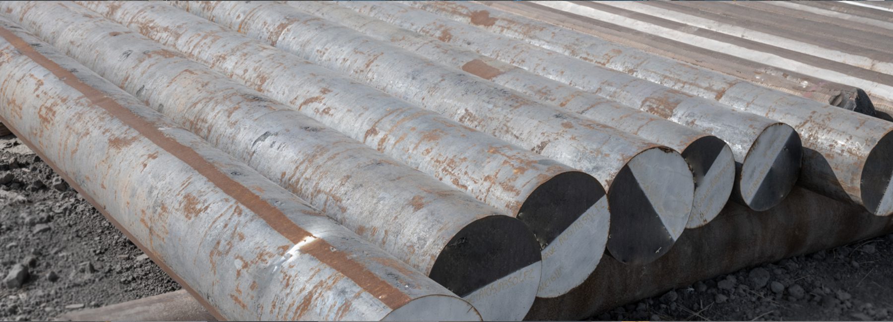 Stacked large metal pipes with rust spots on a gravel surface.