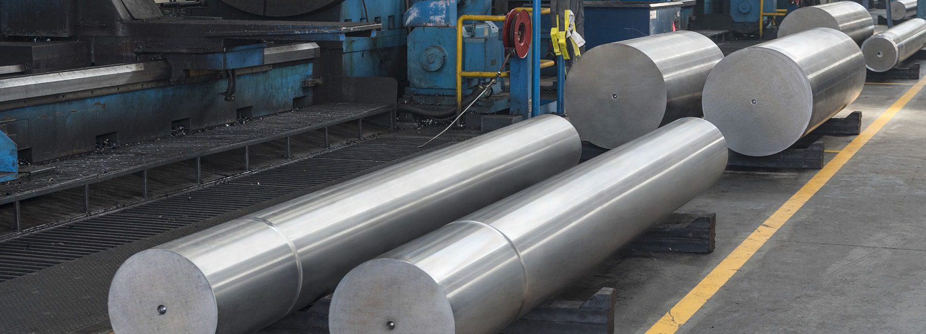 Large cylindrical metal parts on a factory floor, with industrial machinery in the background.