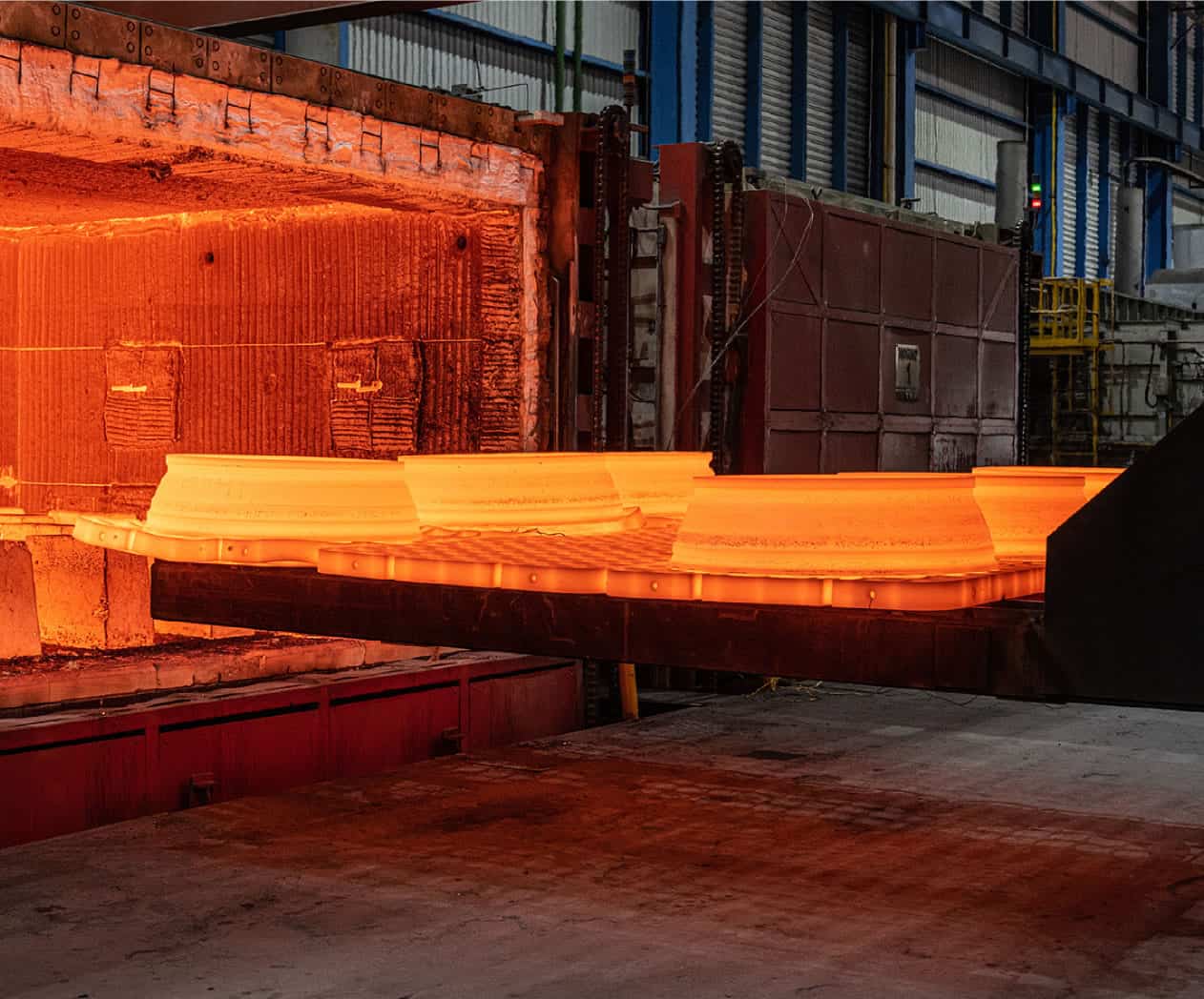 Hot steel slabs glowing orange as they exit an industrial furnace in a steel mill.