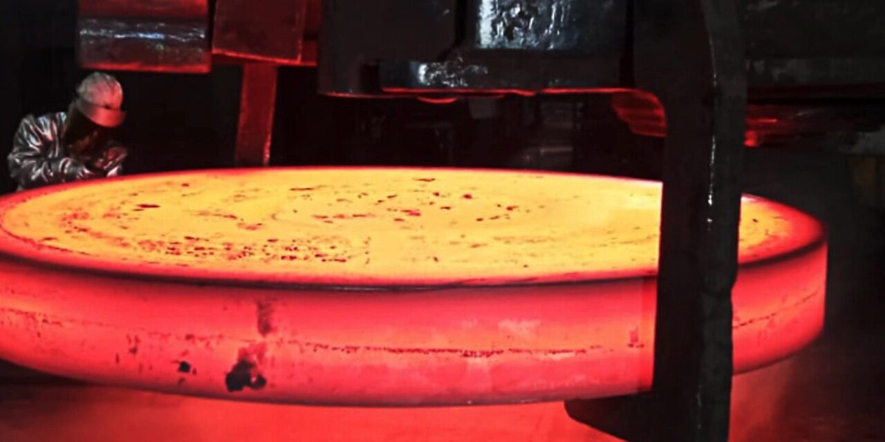 Worker observing large glowing metal disc.